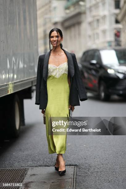Guest wears a black oversized blazer jacket, a low-neck long green silk lustrous dress with floral embroidery, a Dior bag, black pointed shoes,...