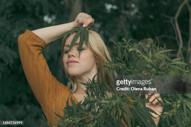 young woman playing with cannabis leaf in a forest. - cannabinoid stock-fotos und bilder