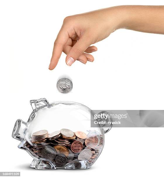 female hand dropping coin into clear half-filled piggy bank isolated - quarter stockfoto's en -beelden