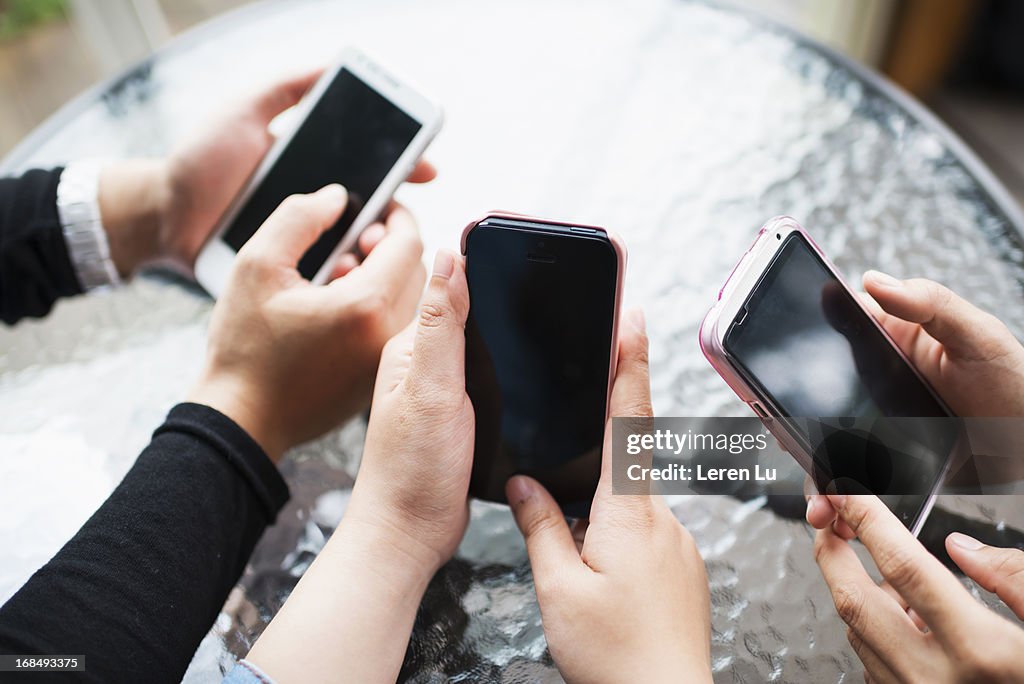 Three girls hold and use smart phones