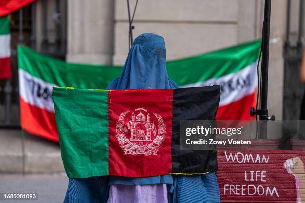 Woman in a burqa holds the flag of Afghanistan to call for freedom for women in the Arab world, next to her a banner with the slogan, women, life and...
