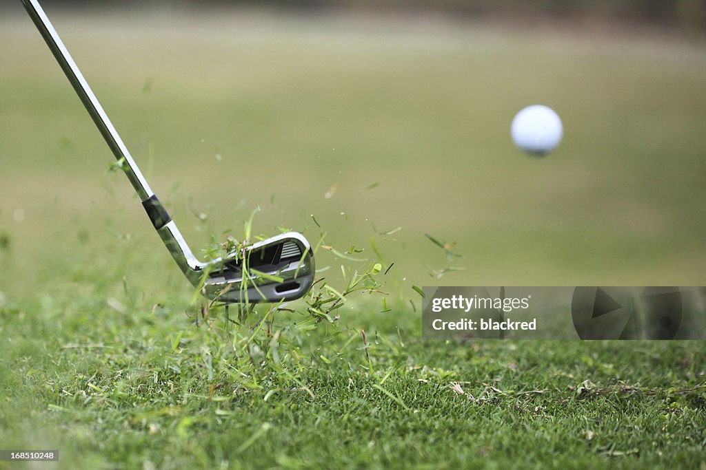 Golf Club Hits Ball in the Air with Grass Flying