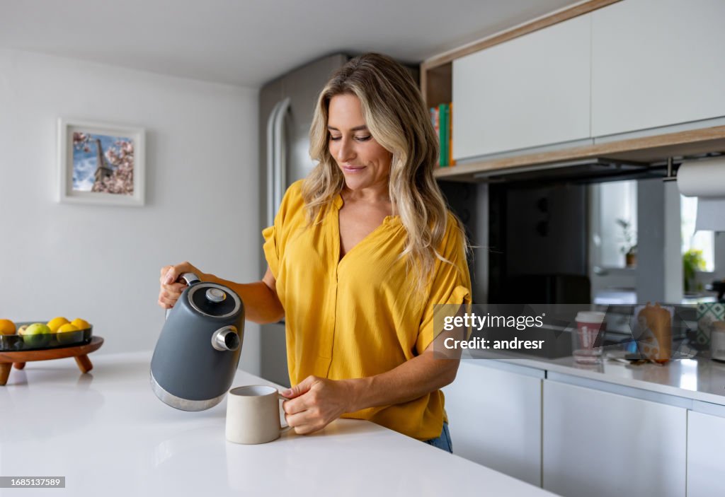 Happy woman at home making a cup of coffee