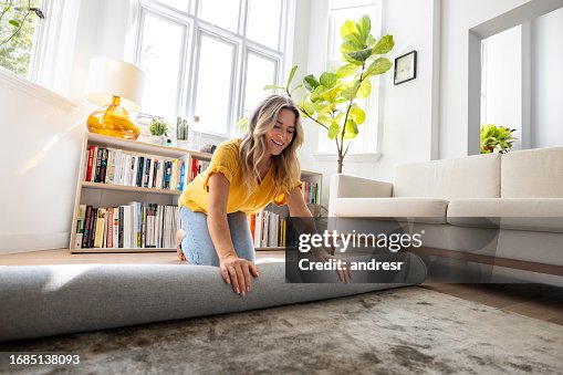 Happy woman moving house and unrolling a carpet while unpacking Happy woman moving house and unrolling a carpet while unpacking