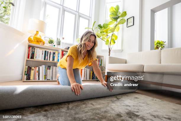 happy woman moving house and unrolling a carpet while unpacking - carpet cleaning stock pictures, royalty-free photos & images