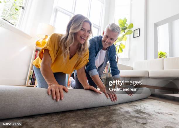 happy couple moving house and unrolling a carpet while unpacking - huisuitbreiding stockfoto's en -beelden
