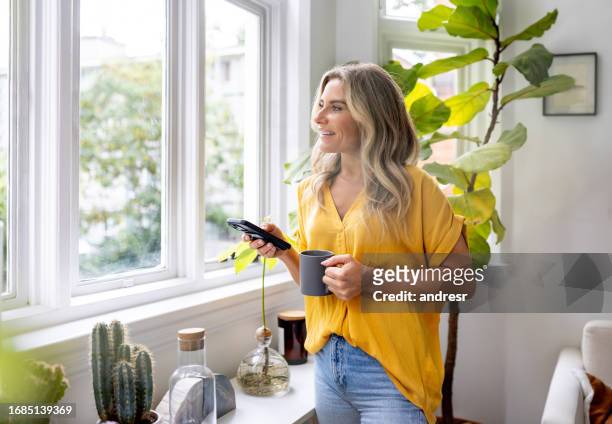 woman at home using her cell phone while drinking coffee - coffee happy stock pictures, royalty-free photos & images