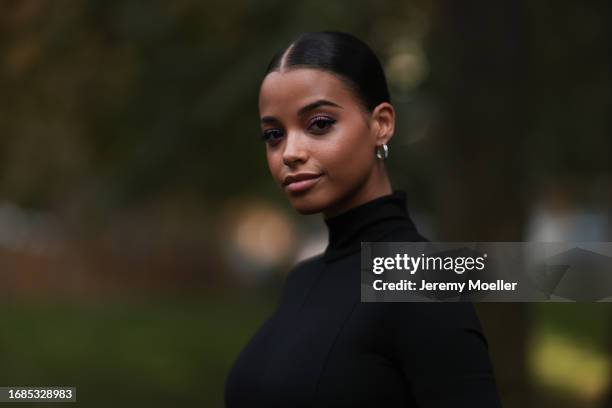 Ella Balinska is seen wearing silver hoop earrings, black sunglasses, a long-sleeved mini dress with turtleneck and purple tulle tutu, black gloves...