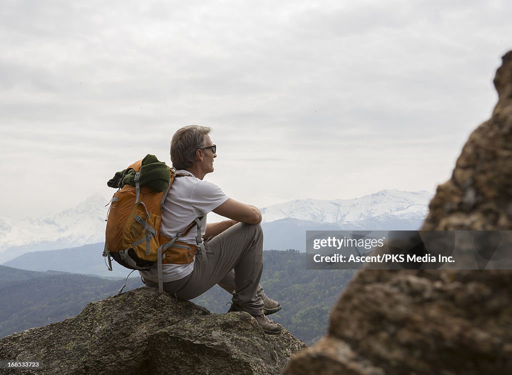 Hiker relaxes on rock above mountains, valley