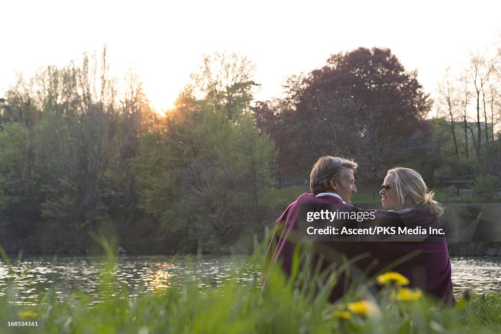 Couple huddle under blanket at river's edge