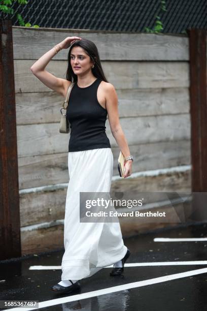 Guest wears a black tank top, a white long skirt, a gray bag, shoes, outside Ulla Johnson, during New York Fashion Week, on September 10, 2023 in New...