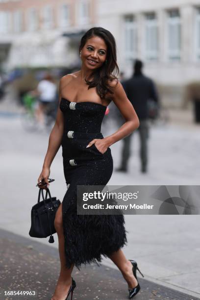 Emma Thynn is seen wearing silver earrings, a strapless black midi dress with fluffy feather hem, sequins, and gemstones details with a Birkin bag...