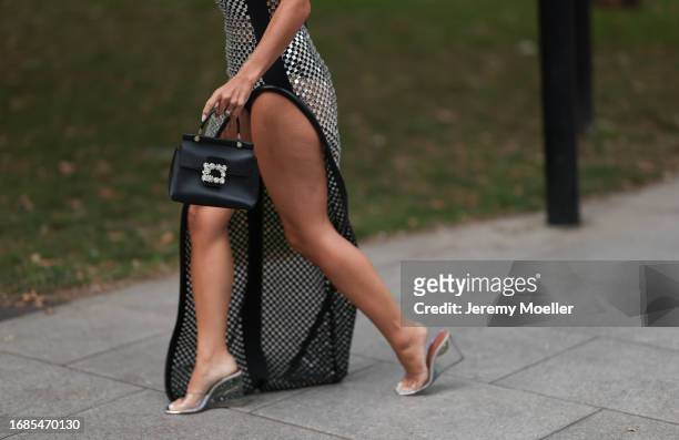 Bettina Looney is seen wearing a see-through maxi dress with side split, consisting of silver shiny squares and black leather straps; a black leather...