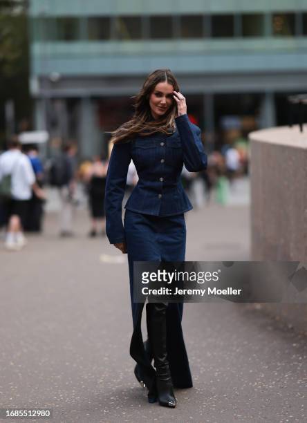 Marianne Fonseca is seen wearing a denim two-piece-set consisting of a buttoned, waisted blazer and a maxi skirt with splits; a golden ring and black...