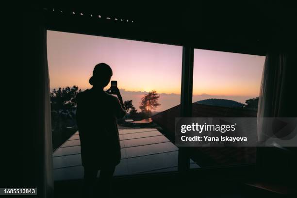 a woman standing in a mountain hotel bedroom using smart phone to take a photo - personal data stock pictures, royalty-free photos & images