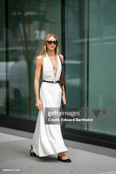 Guest wears sunglasses, a low-neck v-neck white long dress, a belt, flat ballerina shoes, a bag, outside Proenza Schouler, during New York Fashion...