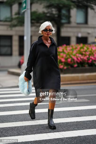 Grece Ghanem wears a long black shirt worn as a dress, a pale pastel blue fluffy bag, black rubber boots, outside Khaite , during New York Fashion...