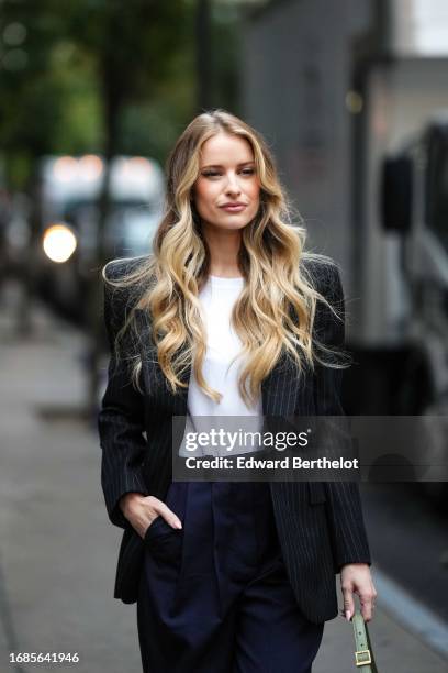 Victoria Magrath wears a striped black and white oversized blazer jacket, a white t-shirt, blue suit pants, a green bag, outside Khaite , during New...