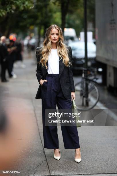 Victoria Magrath wears a striped black and white oversized blazer jacket, a white t-shirt, blue suit pants, white pointed shoes, a green bag, outside...