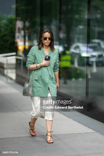 Guest wears sunglasses, a green oversized blazer jacket, a metallic silver shiny Paco Rabanne bag, a skirt, lace up shoes, outside Proenza Schouler,...