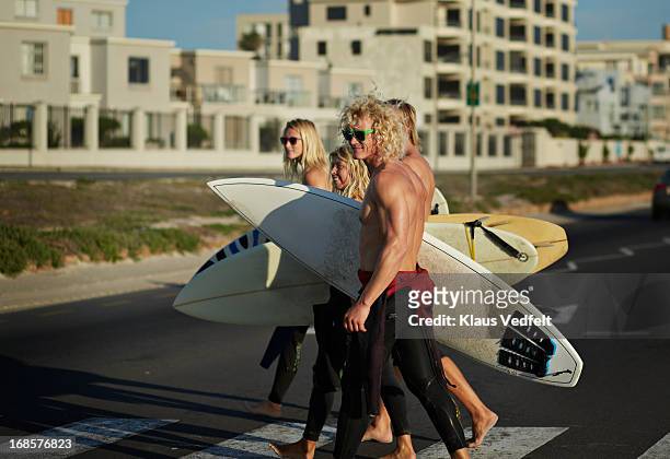 surfers crossing a road holding their surfboards - surfer wetsuit crossed foto e immagini stock