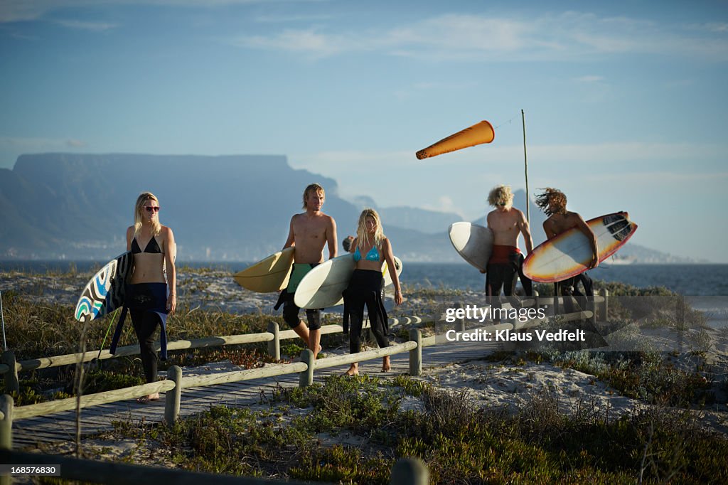 5 surfers walking on boardwalk with surfboards