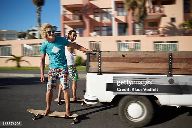 skaters hanging on to car while riding longboards - pieno di risorse foto e immagini stock