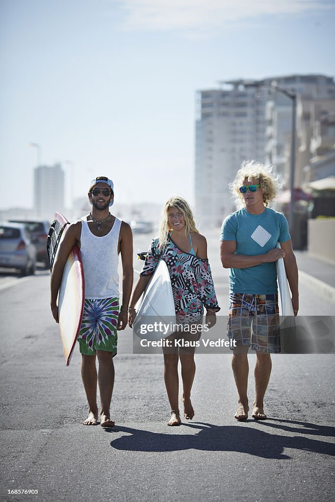 3 surfers walking on road with boards