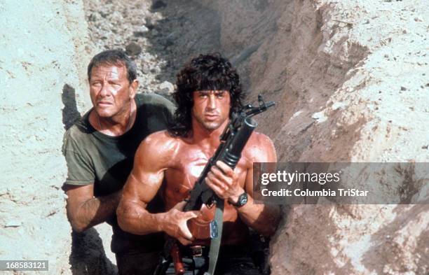 Sylvester Stallone walks through a trench with Richard Crenna in a scene from the film 'Rambo III', 1988.