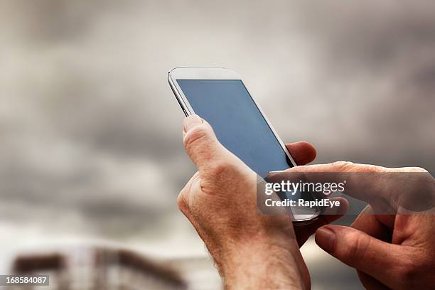 male hand taps touch screen of smart phone in street - tapping stock pictures, royalty-free photos & images