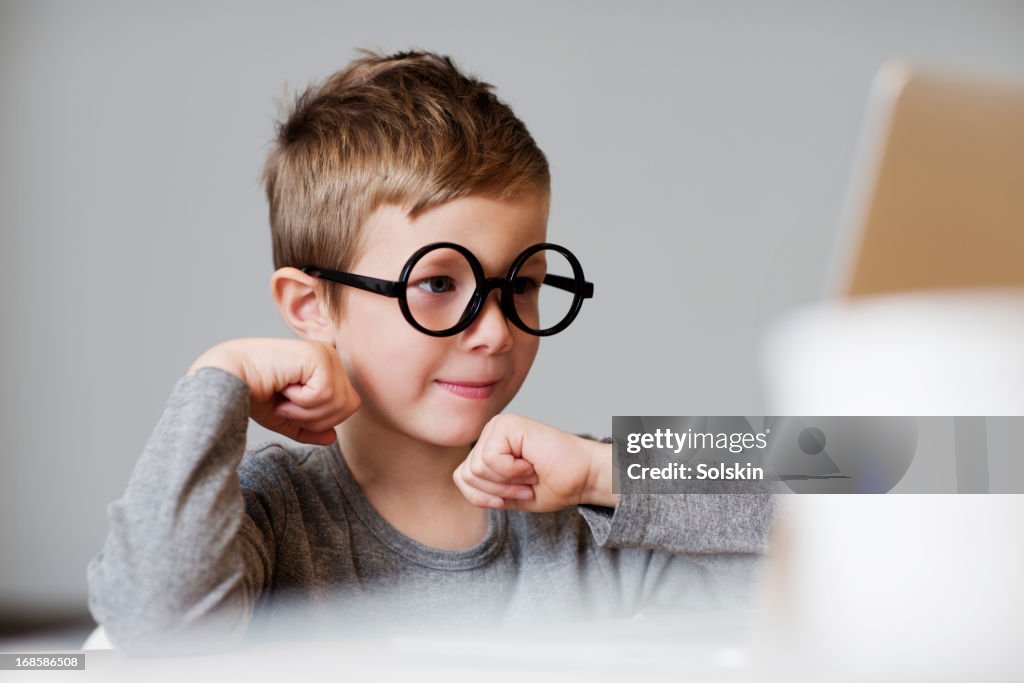 Boy wearing toy glasses using laptop computer