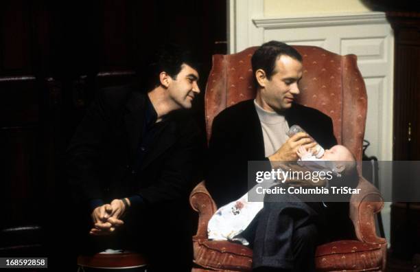 Tom Hanks feeds a baby while Antonio Banderas watches in a scene from the film 'Philadelphia', 1994.