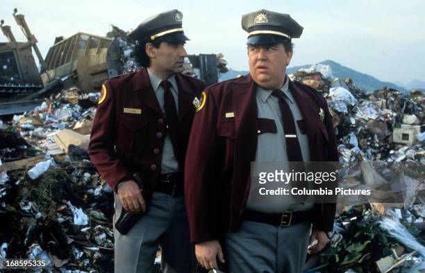 Eugene Levy and John Candy dressed in security guard uniforms while standing in a junkyard in a scene from the film 'Armed And Dangerous', 1986.