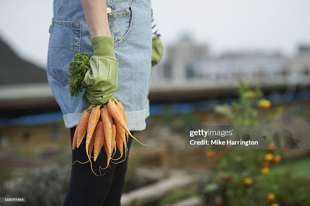 Woman in roof garden holding carrots.