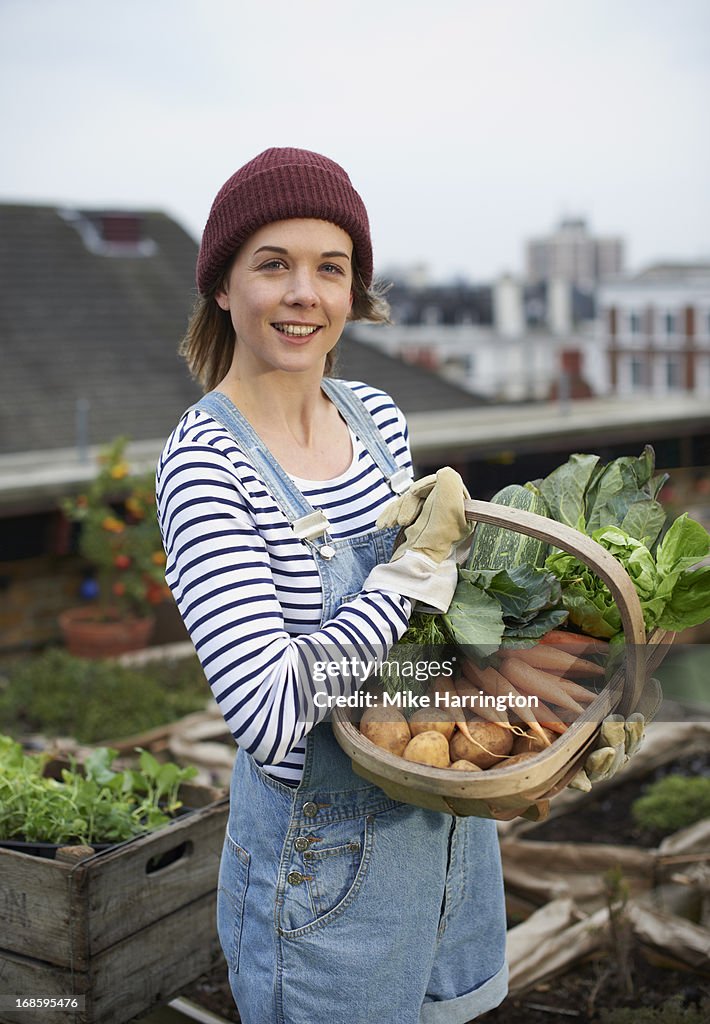 Woman in roof garden holding basket of vegetables.