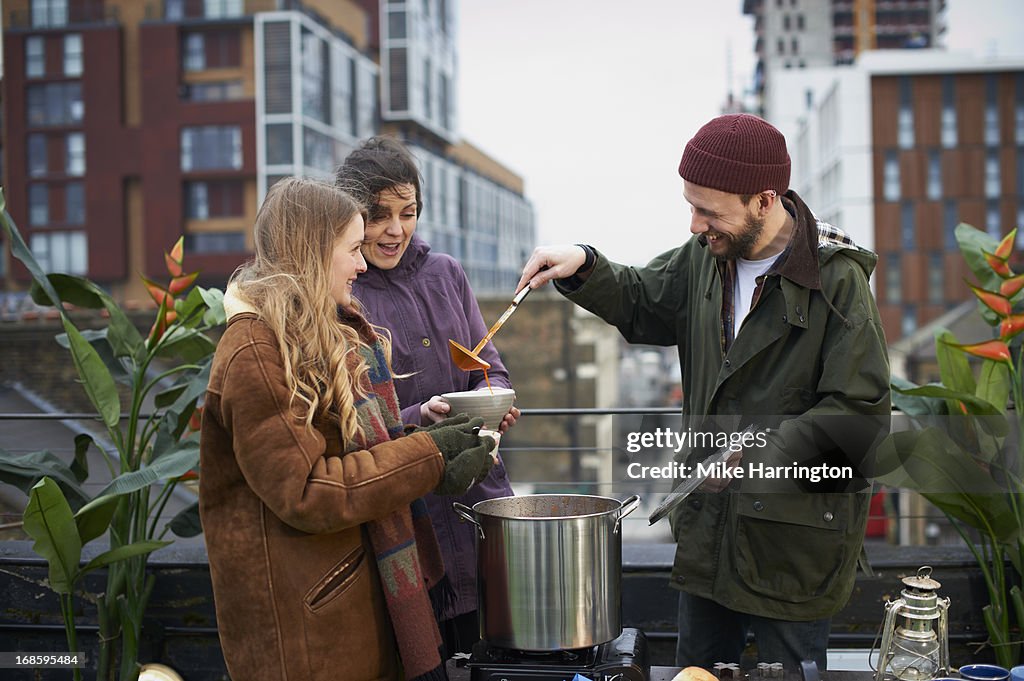 Man pouring soup from pot to friends outdoors.