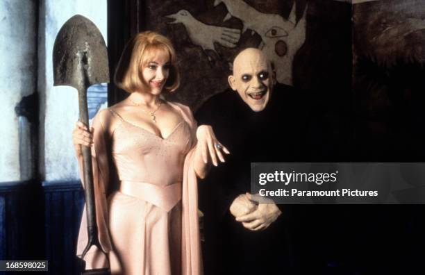Joan Cusack holding shovel next to a smiling Christopher Lloyd in a scene from the film 'Addams Family Values', 1993.