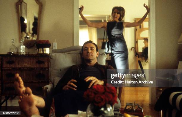 Kevin Spacey lounging in a reclining chair as Annette Bening stands in the entryway perturbed in a scene from the film 'American Beauty', 1999.