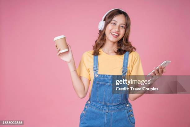 happiness asian smiling young woman wearing technology wireless headphones for listening the music via smartphone or mobile phone isolated over pink background - headphones isolated ストックフォトと画像