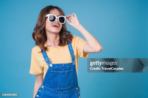 young woman in hat and sunglasses isolated on light blue background. beautiful female in trendy summer clothes. positive model having fun indoors. cheerful and happy - blue white summer hat background stock pictures, royalty-free photos & images