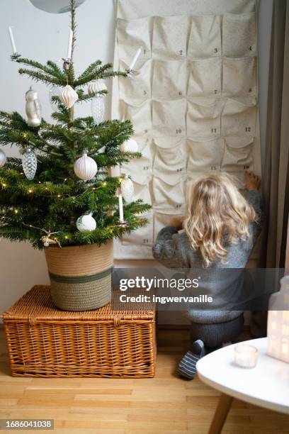 rear view of girl opening christmas advent calendar in the living room near the christmas tree - advent calendar surprise imagens e fotografias de stock