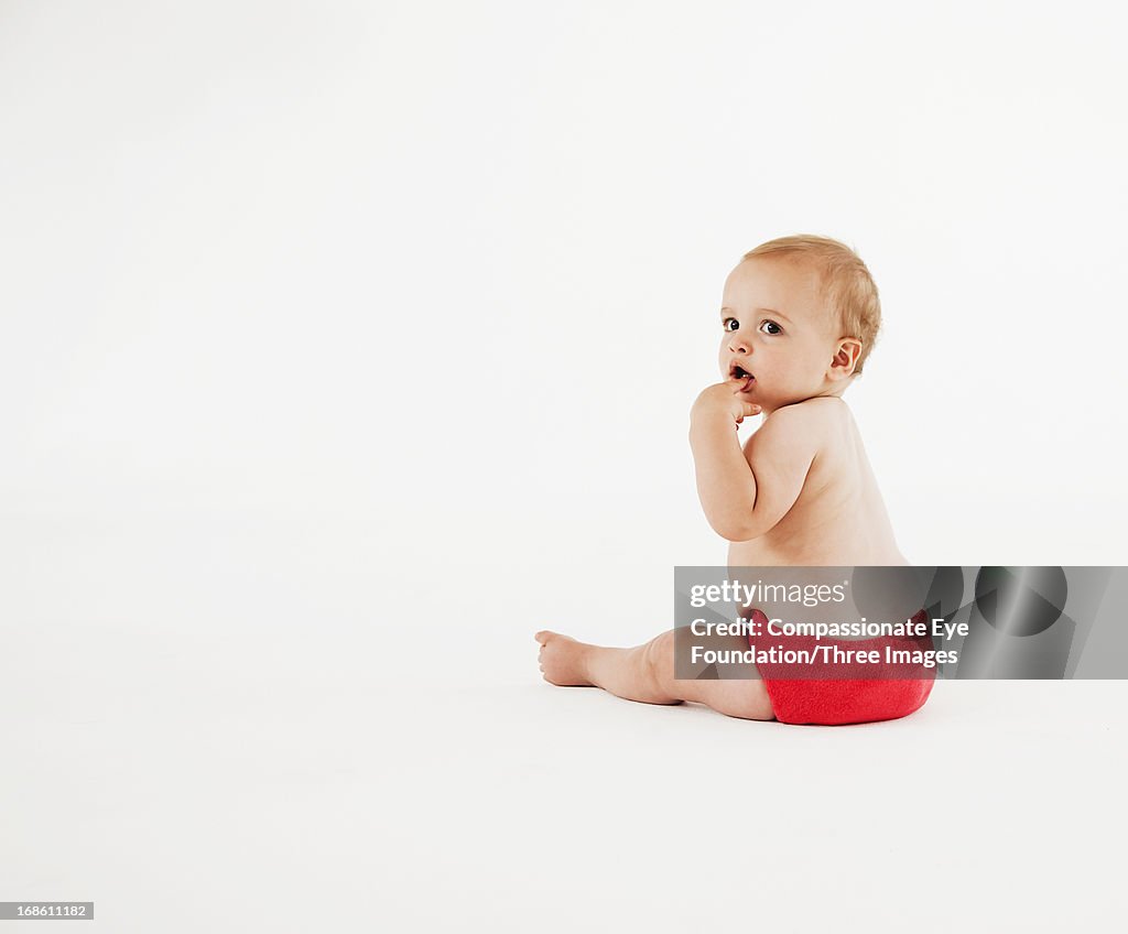 Baby sitting on floor with finger in mouth