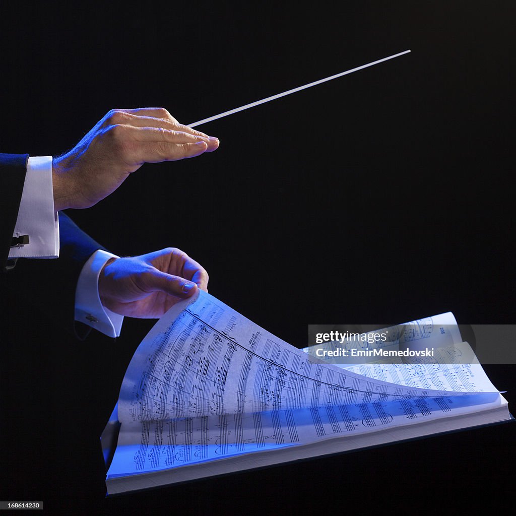 Hands of a conductor with a baton and musical book