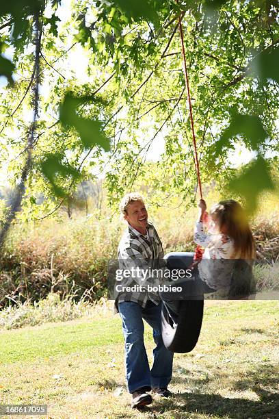 father pushing daughter on tire swing - tire swing stock pictures, royalty-free photos & images