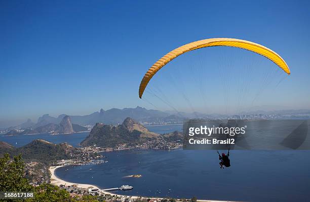 a person paragliding over calm blue sea in rio de janeiro  - niteroi stock pictures, royalty-free photos & images