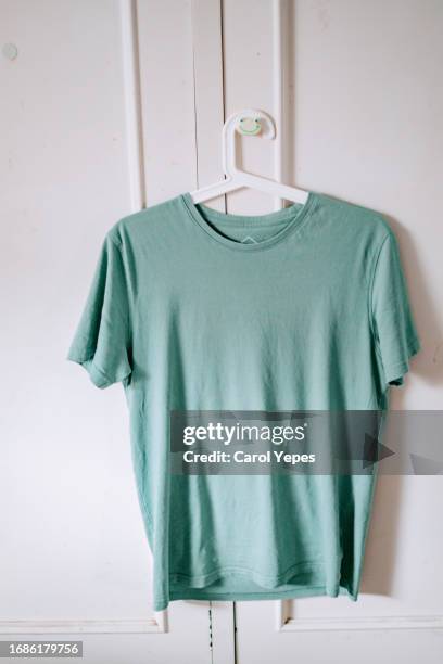 green t-shirt  hanging in hanger against white wall - hanging blouse stock pictures, royalty-free photos & images