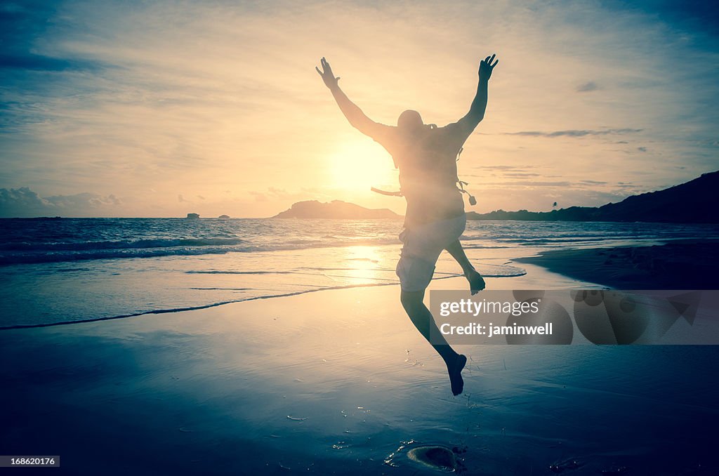 Mann springen am Strand gegen Morgen Sonnenstrahl