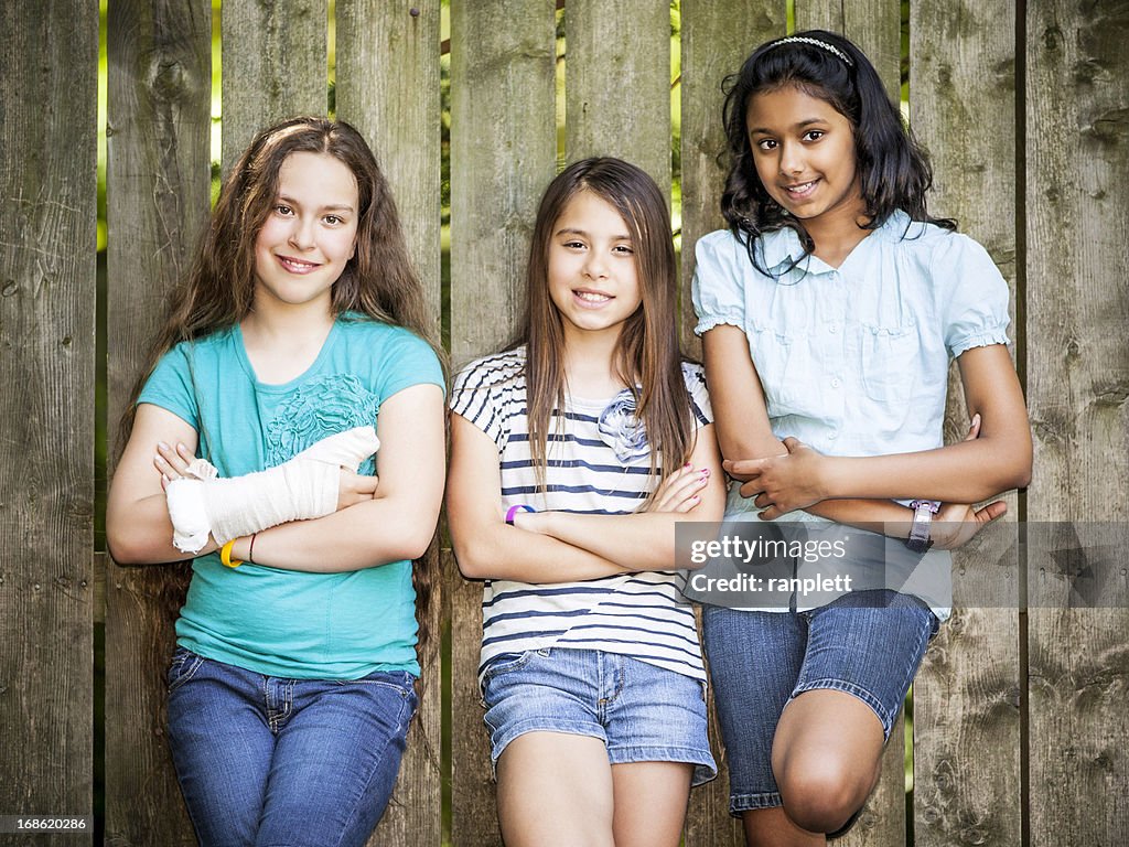 Three smiling Pre-Teen Girls Leaning Against a Fence