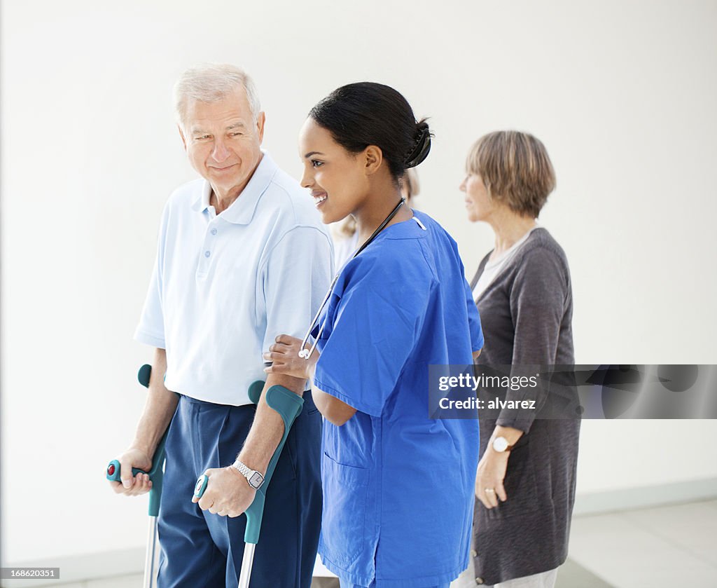 Enfermera ayudar a un paciente senior en crutches