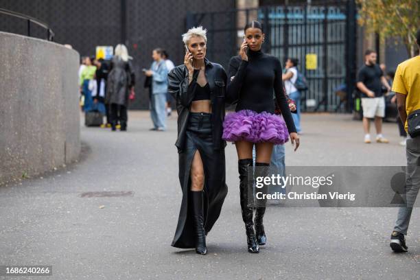 Wallis Day wears black skirt with slit, coat, cropped top & Ella Balinska wears purple ruffled skirt, black long sleeve, over knees boots outside...